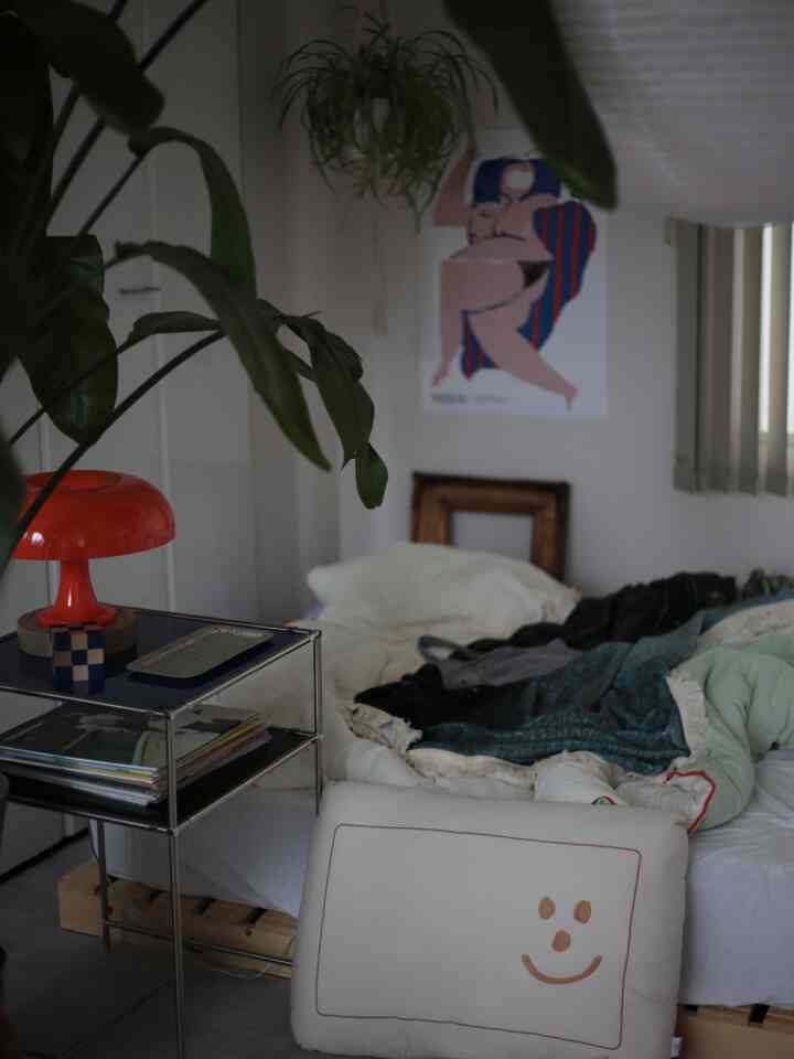 White-toned bedroom featuring plants by the window and an orange table lamp on the side, with a natural and minimalist atmosphere
