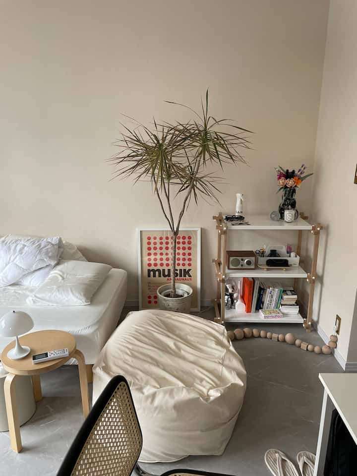 Natural-tone single household living room featuring a large beige bean bag, wood-toned shelving, and a poster in a cozy setting