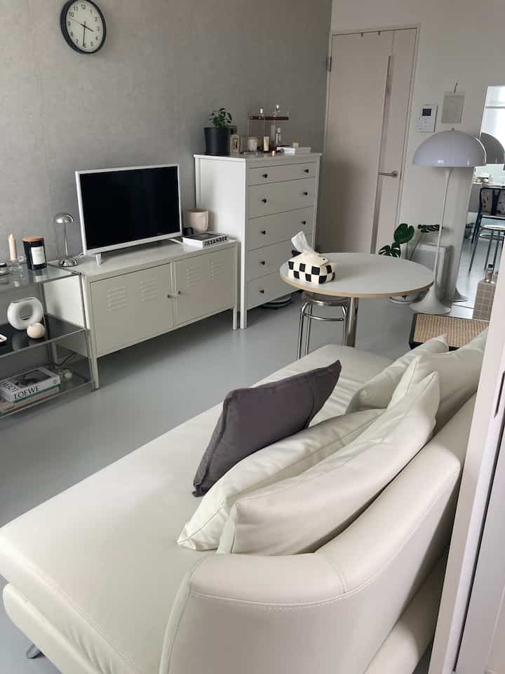 白とグレーのトーンのリビング、ホワイトのソファとキャビネット、丸テーブルが配置されたモダンでシンプルなインテリア