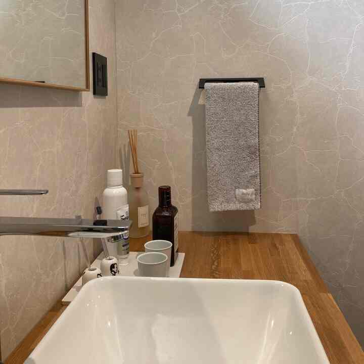 アイボリーベージュの壁と木製カウンターが調和するバスルームの洗面台、グレーのタオルが黒いタオル掛けにかかっている