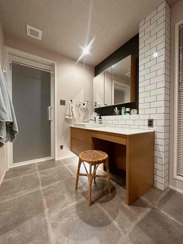 ナチュラルな色調と白いタイルが調和するパウダールーム、木製のスツールとすっきりした収納家具が配置された実用的な空間