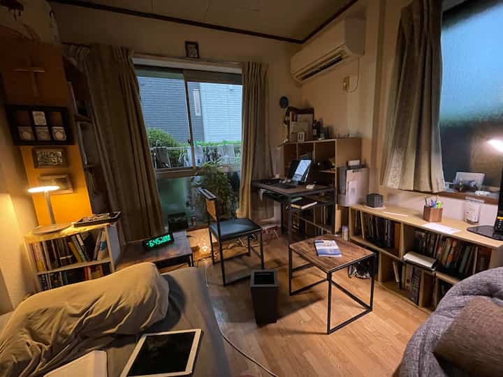 Warm wood tones and beige curtains in a small living room with a home office setup, featuring a desk and sofa in a cozy atmosphere