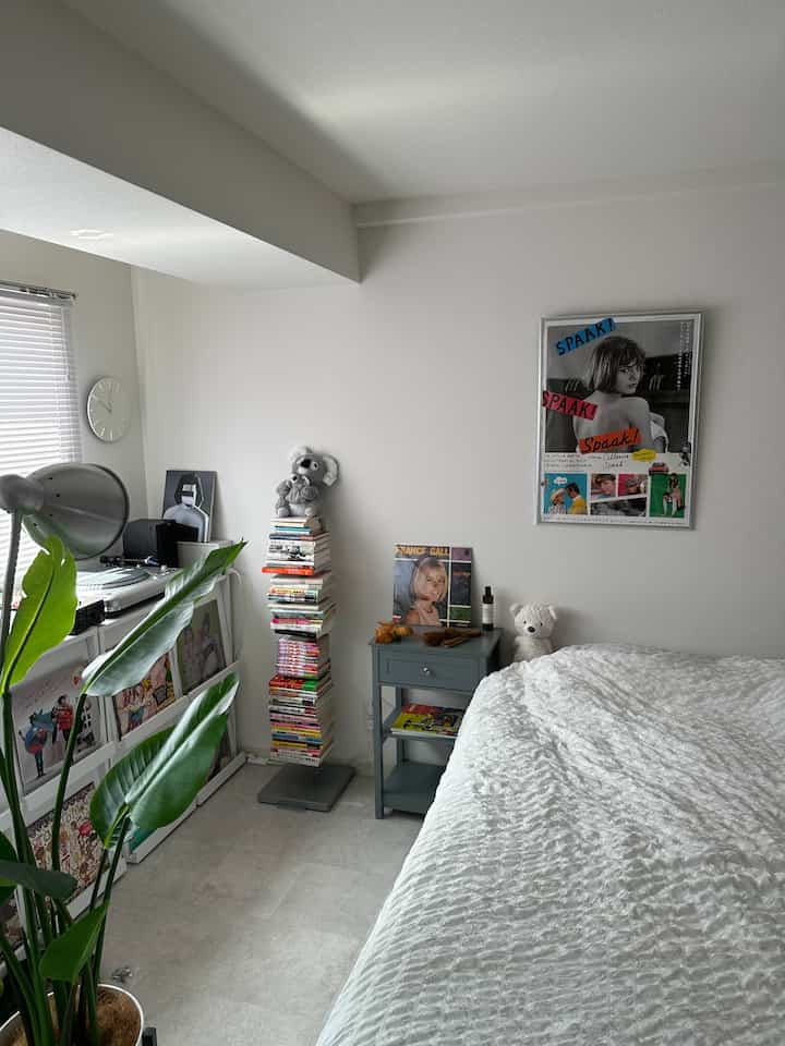 明るい白を基調とした寝室、ベッドとナイトテーブル、本棚、観葉植物が配されたシンプルで落ち着いたインテリア