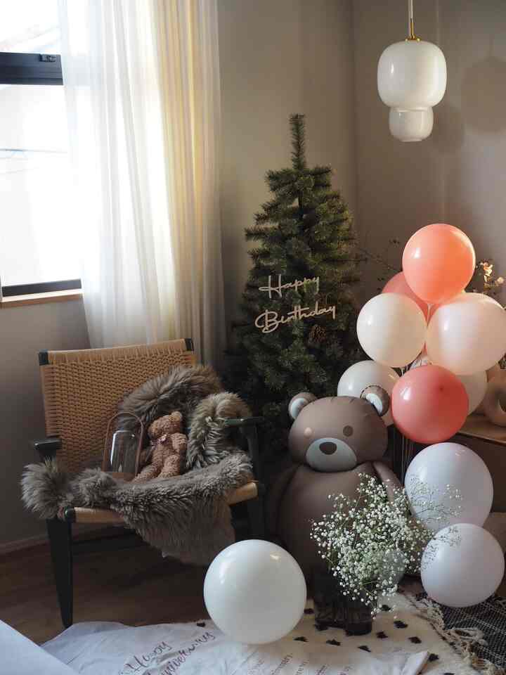 ピンクと白を基調とした子供部屋に、風船とクリスマスツリー、テディベアが配置された温かみのある誕生日のお祝い空間