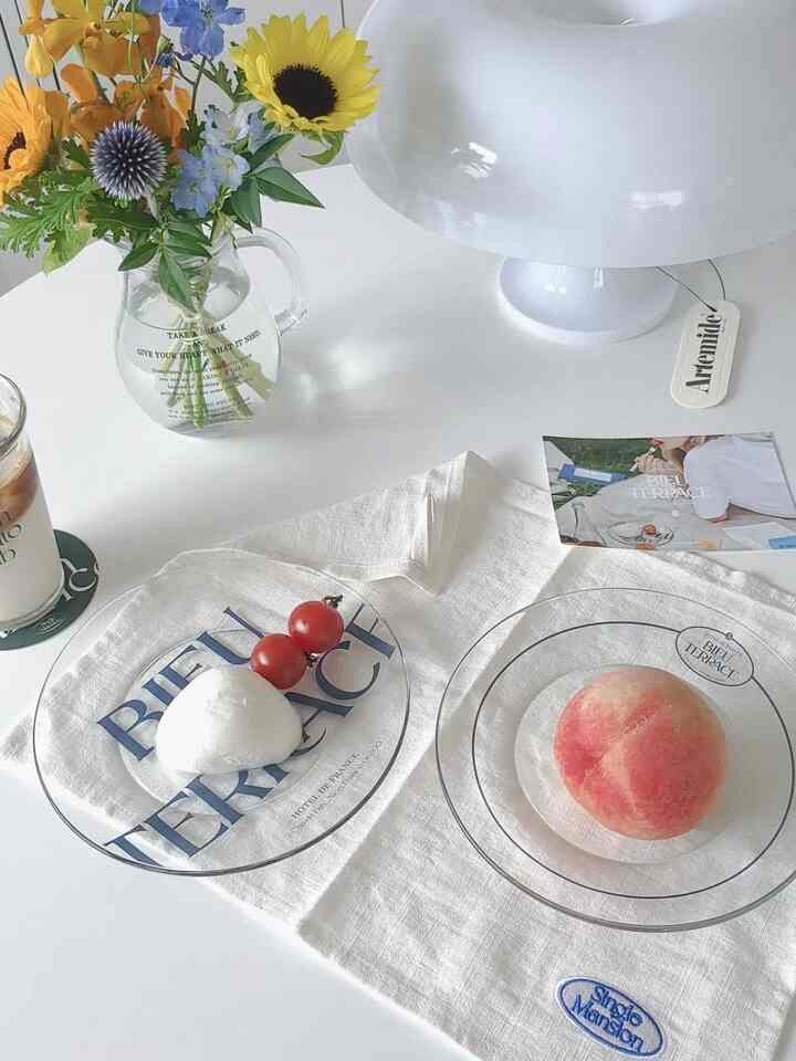 白を基調としたダイニングテーブルに透明な皿と花瓶が置かれた、清潔感のあるインテリア