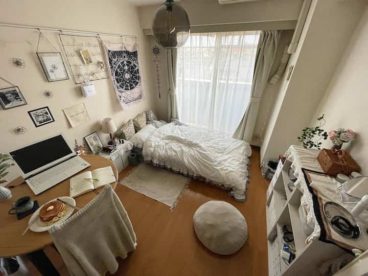 Compact studio in white and brown tones featuring a bed and desk with cozy, personal touches
