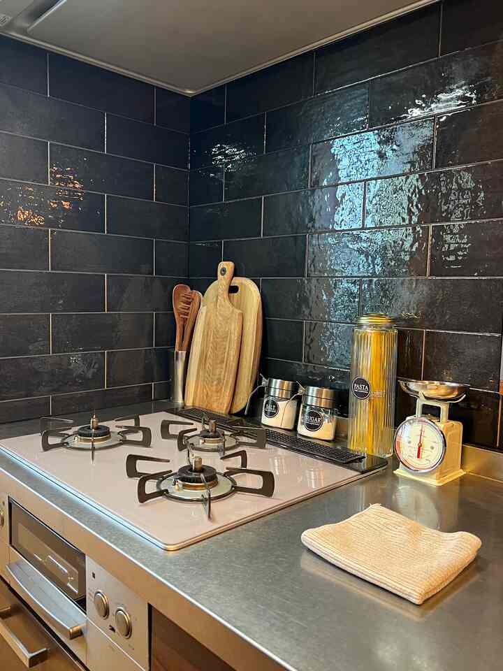 シルバーのステンレスキッチンカウンターと黒いタイルの壁、木製のまな板や調理器具が配置された清潔感のある印象的なキッチン