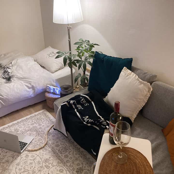 白と緑の色調のリビング兼寝室、ソファとベッド、フロアランプ、ネオンクロックがある雰囲気のある韓国風インテリア