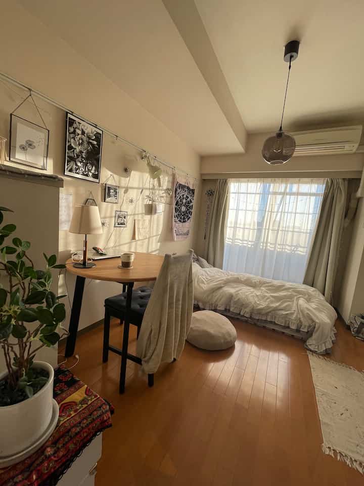 Natural color tone studio bedroom featuring a bed, round dining table, and beige curtains with a cozy atmosphere