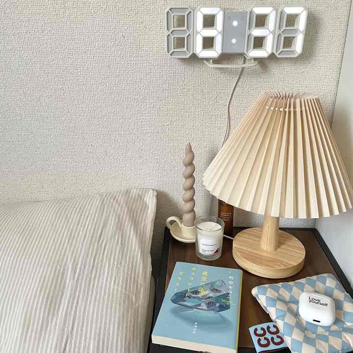 白と木目調の寝室のナイトテーブル、読書用の本とテーブルランプ、キャンドルが配置された落ち着いた雰囲気のインテリア