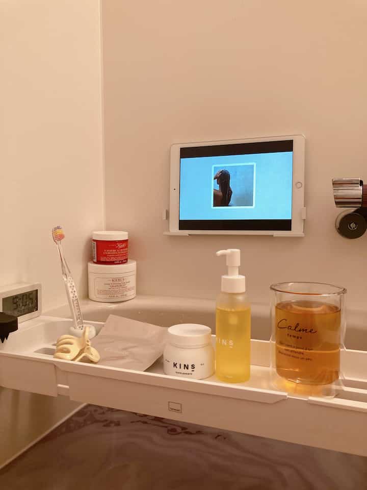 白を基調としたバスルームに配置されたバスタブトレイとスキンケア用品、デジタル時計がある落ち着いた雰囲気のインテリア