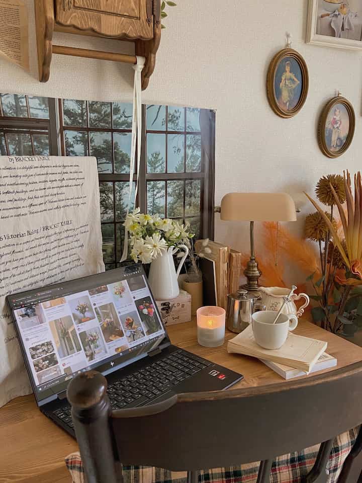 A natural color and wood tone home office space featuring a desk with a vase of flowers, candle, and table lamp creating a warm, cozy atmosphere