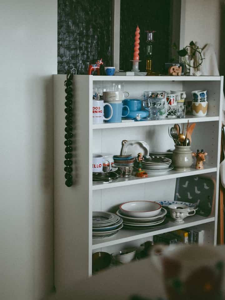 白を基調とした一人暮らしのキッチンスペース、ヴィンテージ食器が並ぶ整った本棚が印象的な雰囲気のあるインテリア