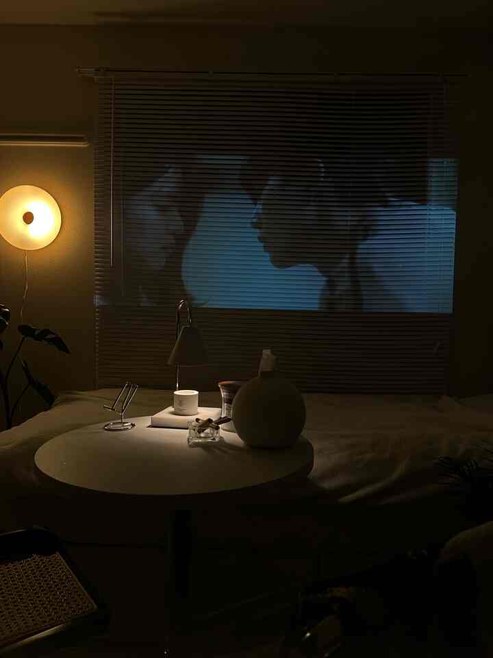 A natural bedroom with dim lighting and warm yellow wall lamp, featuring a movie projected on blinds for a cozy atmosphere