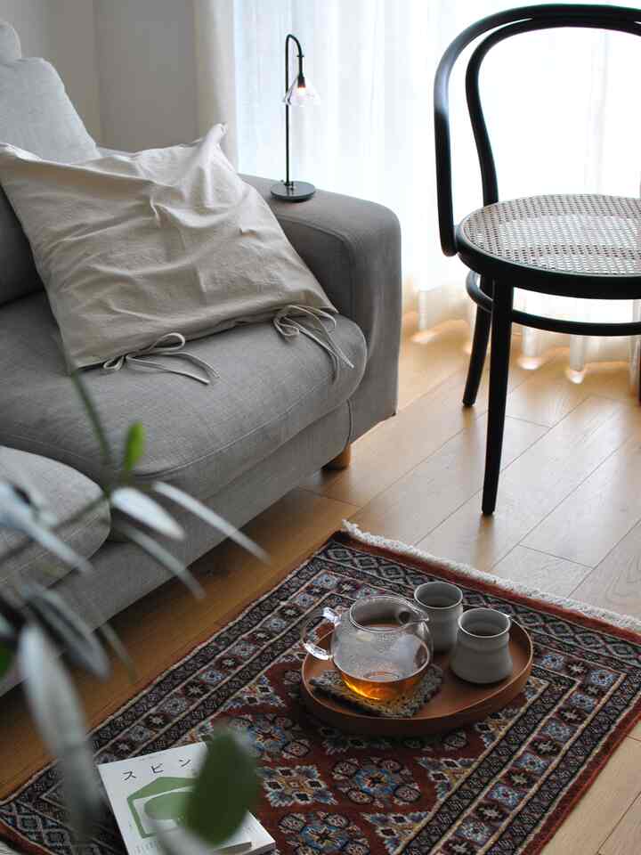 ナチュラルな色調のリビング、グレーのソファとベージュのクッション、木製トレイに置かれたティーセットがある雰囲気のある空間