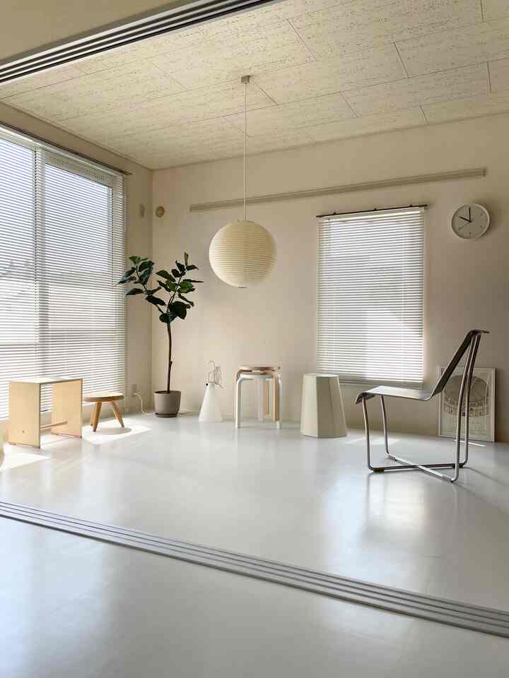 明るいホワイトトーンの正方形リビング、天井中央の丸いペンダントライトと木製スツール、植物が配置されたミニマルな空間