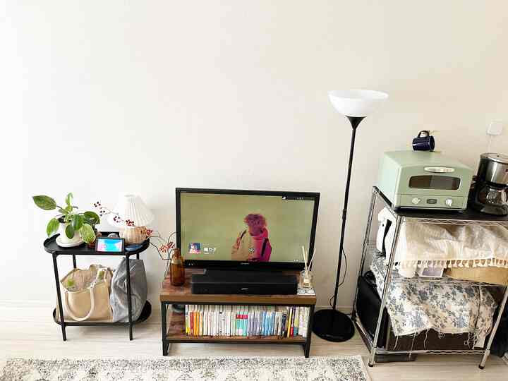 White-walled living room featuring wood tone furniture, a black floor lamp, and a multifunctional kitchen cart with a simple natural vibe