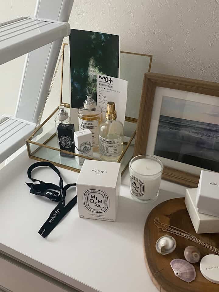 白いテーブルトップにキャンドル、香水、額縁、木製トレイが配置された雰囲気のあるインテリア空間