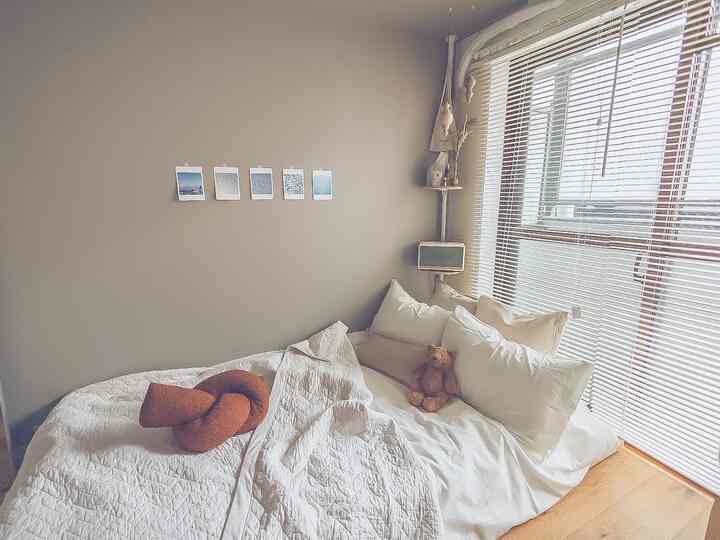 ベージュの壁と木製の床が特徴の寝室、白い寝具とクッション、壁に掛けられた写真がある雰囲気のある空間