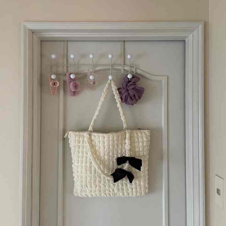 Clean storage space with pink and purple hair accessories and an ivory bag hanging on a white door