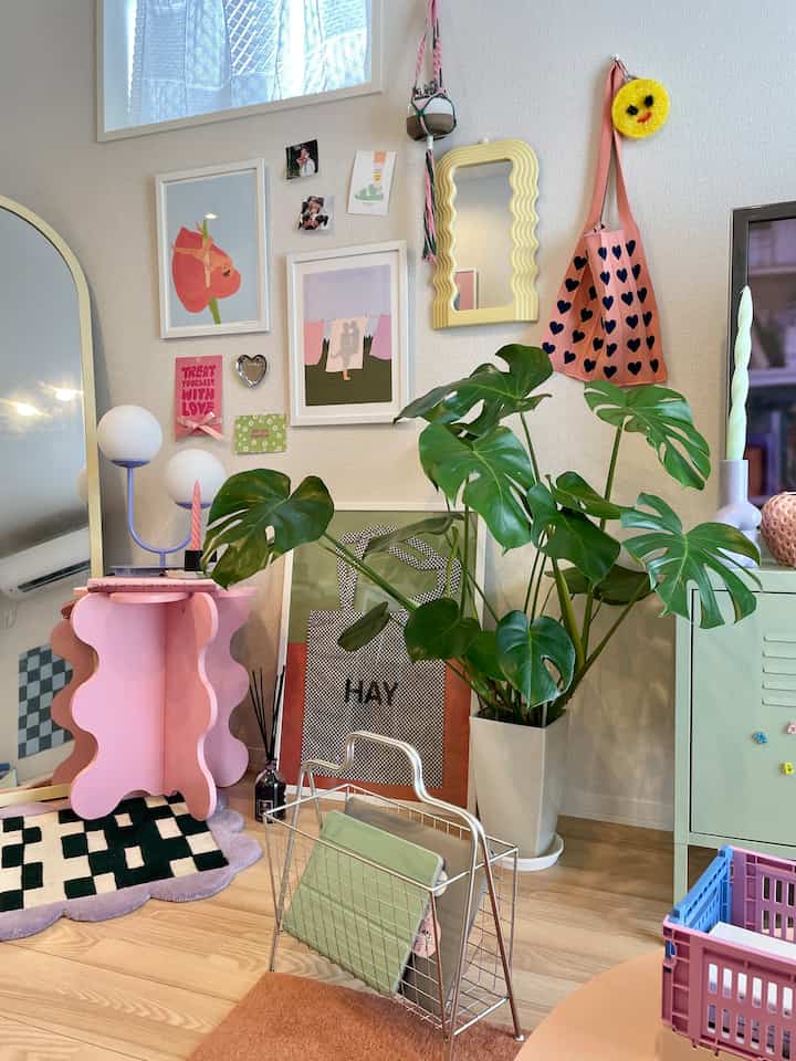 ピンクとナチュラルトーンが調和するリビング、植物やカラフルな壁飾り、ユニークな家具が配置された雰囲気のある空間