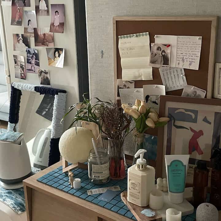 A white and blue toned space featuring a memo board, vases with flowers, and neatly arranged cosmetics, creating a cozy atmosphere.