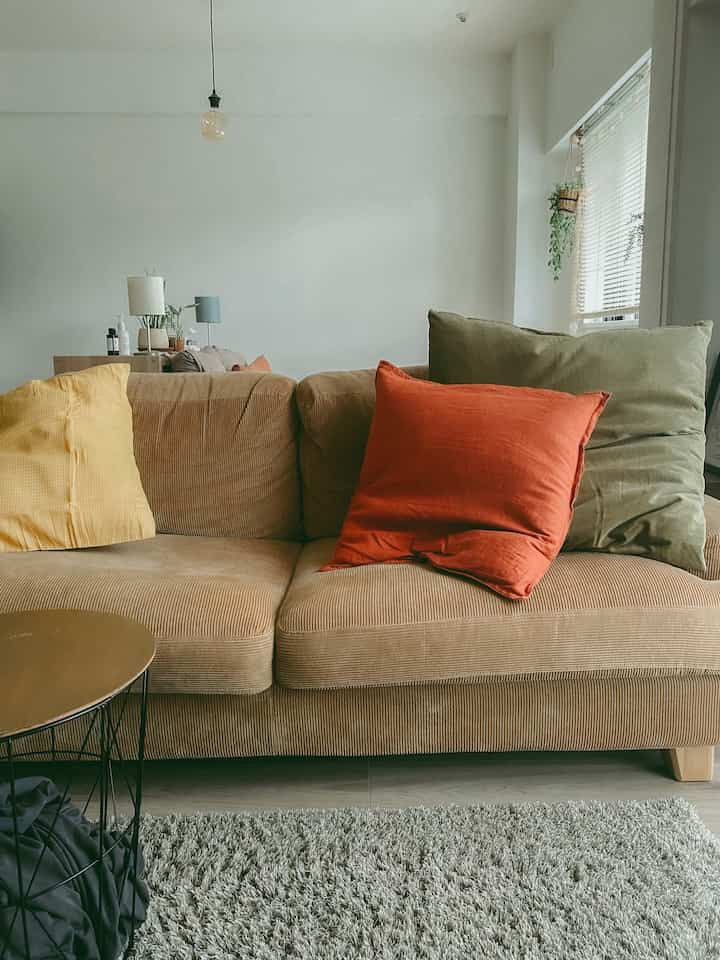 ベージュ調のリビング、コーデュロイ素材のソファとカラフルなクッションが配置されたシンプルで自然な雰囲気のインテリア