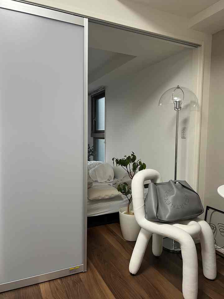 白と木目調のコンパクトな1DK空間、スライディングドア、フロアランプ、ソファベッドが配置された自然で落ち着いたインテリア