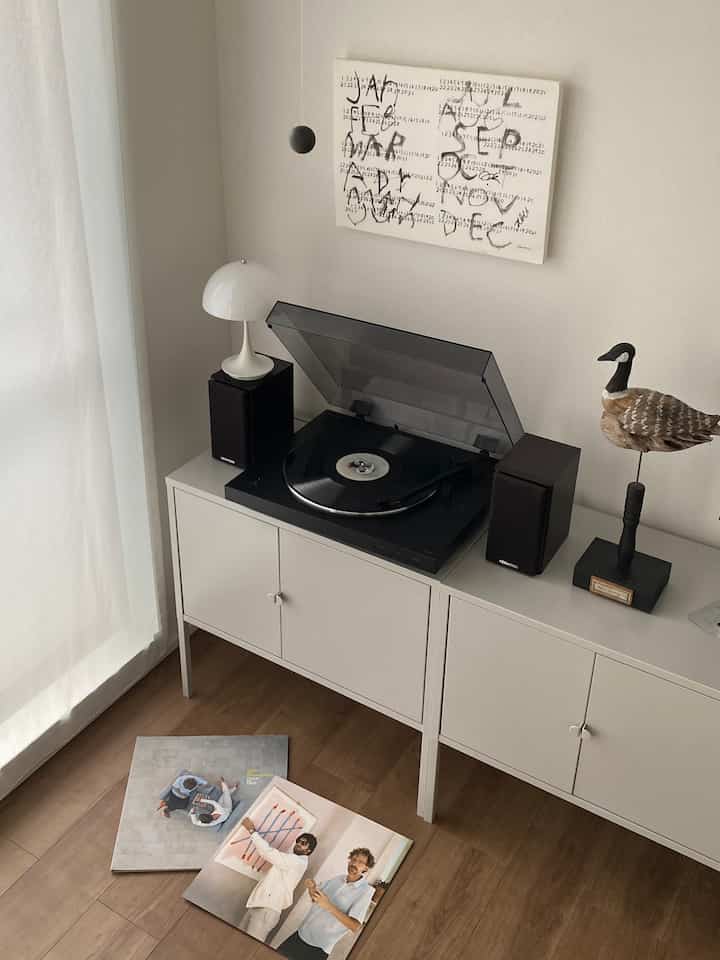 白い家具と茶色い木の床が調和するリビング、中央にターンテーブルとスピーカーが配置された雰囲気のある空間