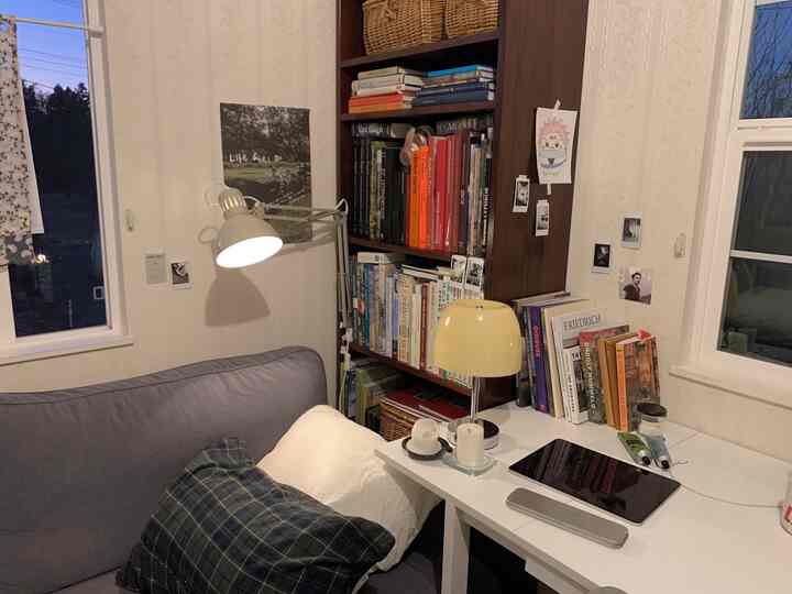 ベージュとグレーの落ち着いた色調のリビング、書棚とソファ、作業用のデスクが配置された雰囲気のある空間