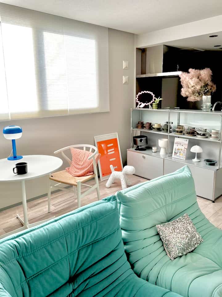 Bright-toned living room featuring a mint sofa, white armchair, and a metal sideboard with decorative cups