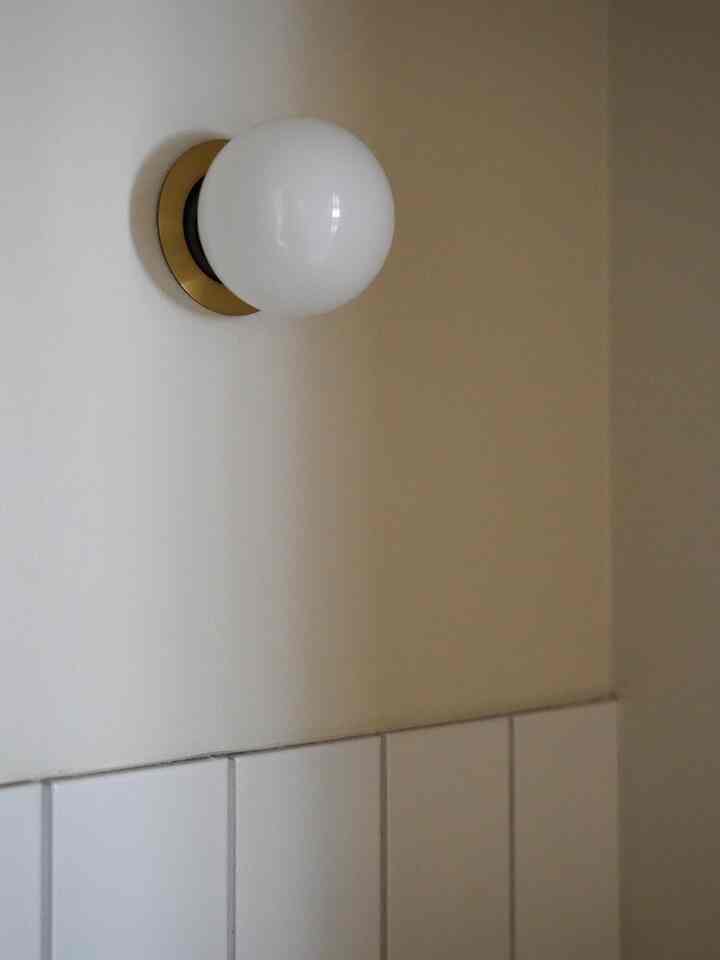 Bathroom wall light featuring a gold ring and white globe shade on beige wall with white tiles, creating a cozy atmosphere