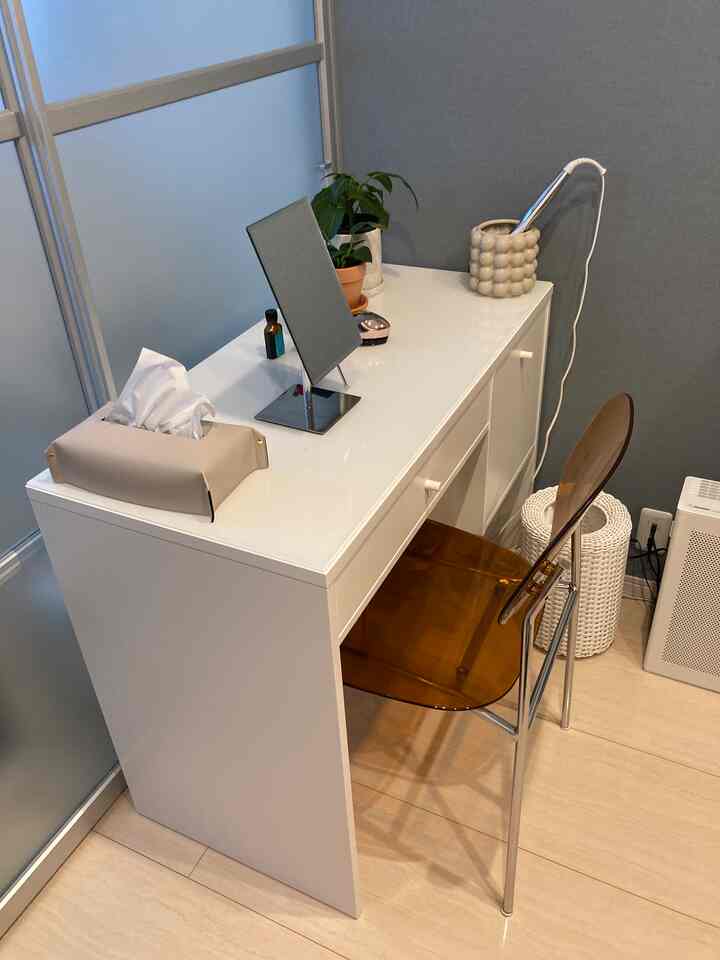 White-tone compact vanity space featuring a brown transparent chair and a green plant in a clean interior