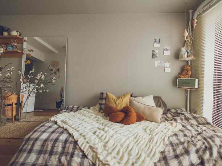 ベージュ色の壁と白い掛け布団カバーがある8畳のワンルーム、ナチュラルでシンプルな雰囲気のベッド中心の空間