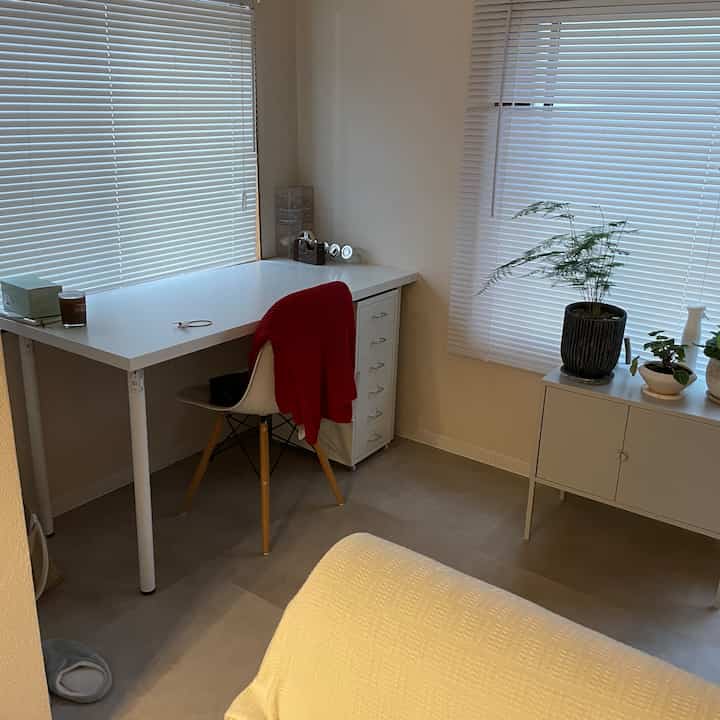 Small home office room in white and natural tones featuring a white desk, chair, and storage units with a simple and clean atmosphere