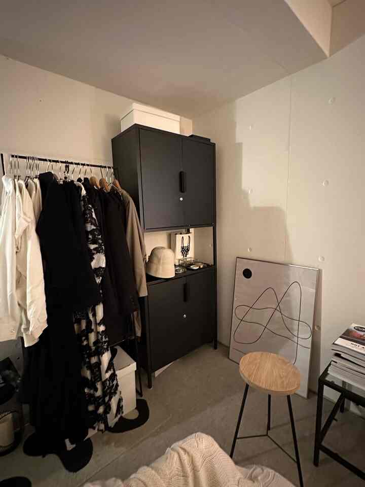 Modern narrow room featuring a black cabinet, clothes rack, and wooden stool with minimalist decor