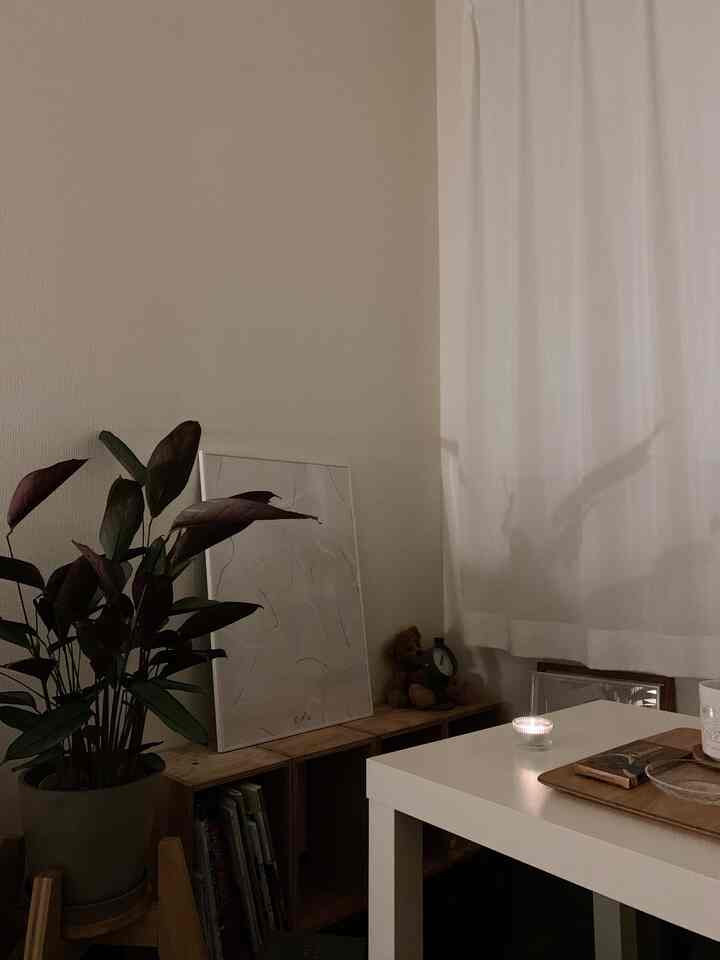 ベージュの壁と白いカーテンのナチュラルリビング、植物と木製の装飾、テーブルの上のキャンドルが雰囲気のある空間を演出しています