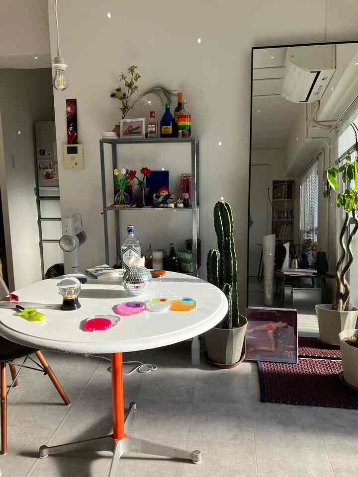 Bright living room with white walls and a vivid orange table leg accent, featuring mirror and plants bathed in natural light