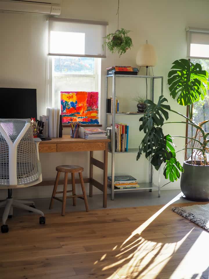 明るく自然な色調のワークスペース、デスクとオフィスチェア、棚と植物が配置された雰囲気のある空間