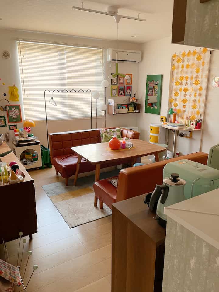 オレンジとグリーンのトーンが特徴のミッドセンチュリーモダンなリビング、ブラインドのある窓辺と木製のダイニングテーブル、ソファが配置された雰囲気のある空間