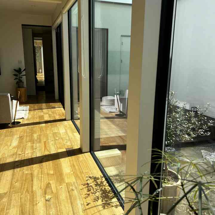 暖かみのある木目調の床と透明な窓が特徴のリビング、中庭が見えるナチュラルモダンな空間