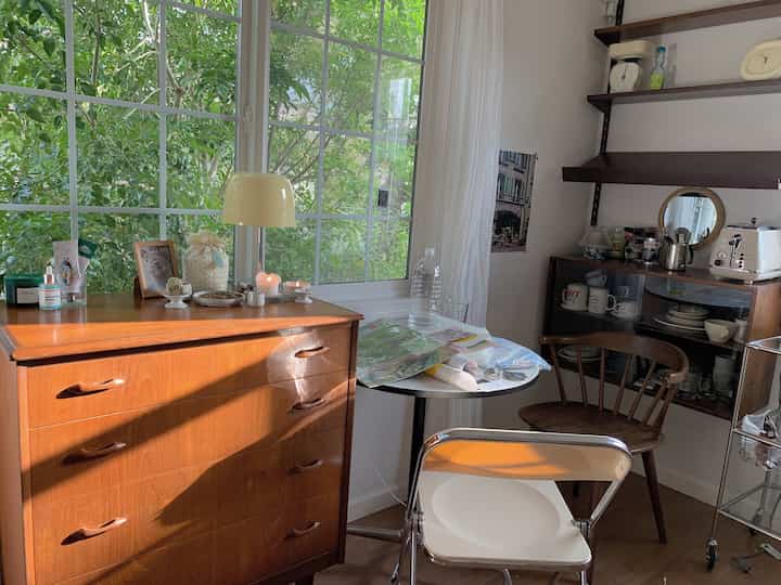 温かみのあるブラウンとホワイトの色調の狭いダイニングルーム、木製チェストと丸テーブル、カーテンが配された雰囲気のある空間