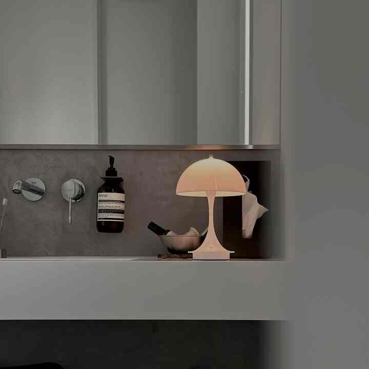 白とグレーのトーンのバスルーム化粧台、ほのかな光を放つパンテラテーブルランプが置かれたモダンなインテリア