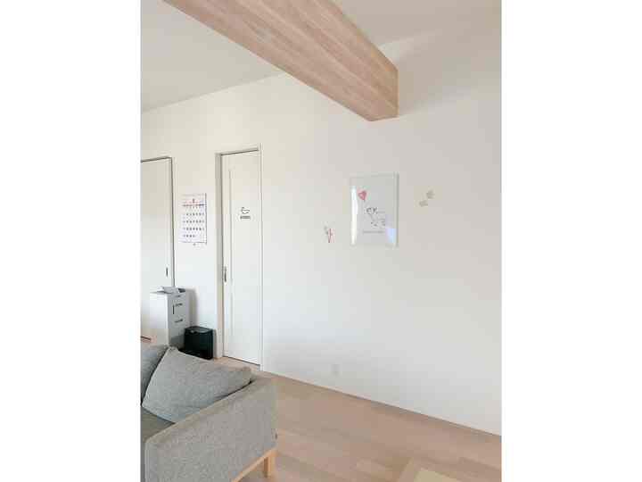 白と木目調が調和したリビング、グレーのソファと犬のポスターが配置された清潔感のある空間