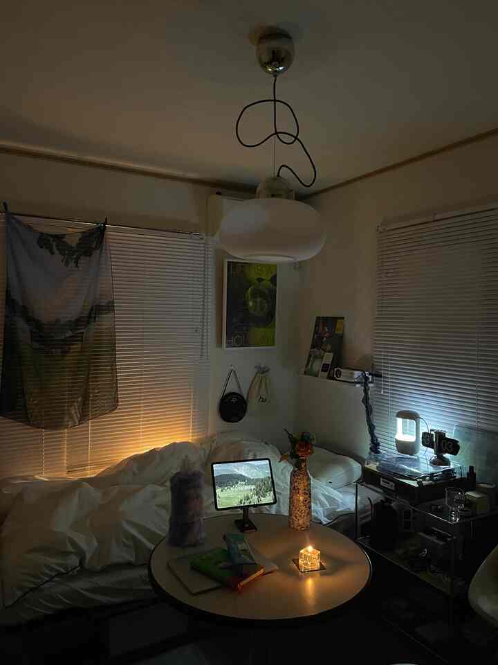 A small living room in white and natural tones, featuring blinds and a candle creating a cozy nighttime ambiance