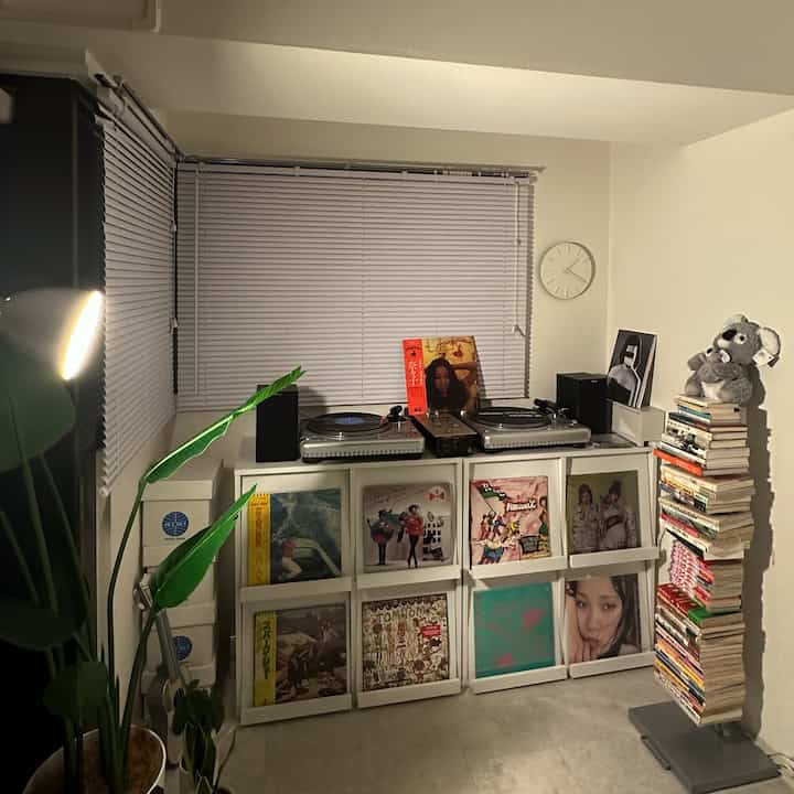 ホワイトを基調とした音楽空間、ブラインドとフロアランプ、ディスプレイラックに並んだLPと本が配置された雰囲気のあるインテリア