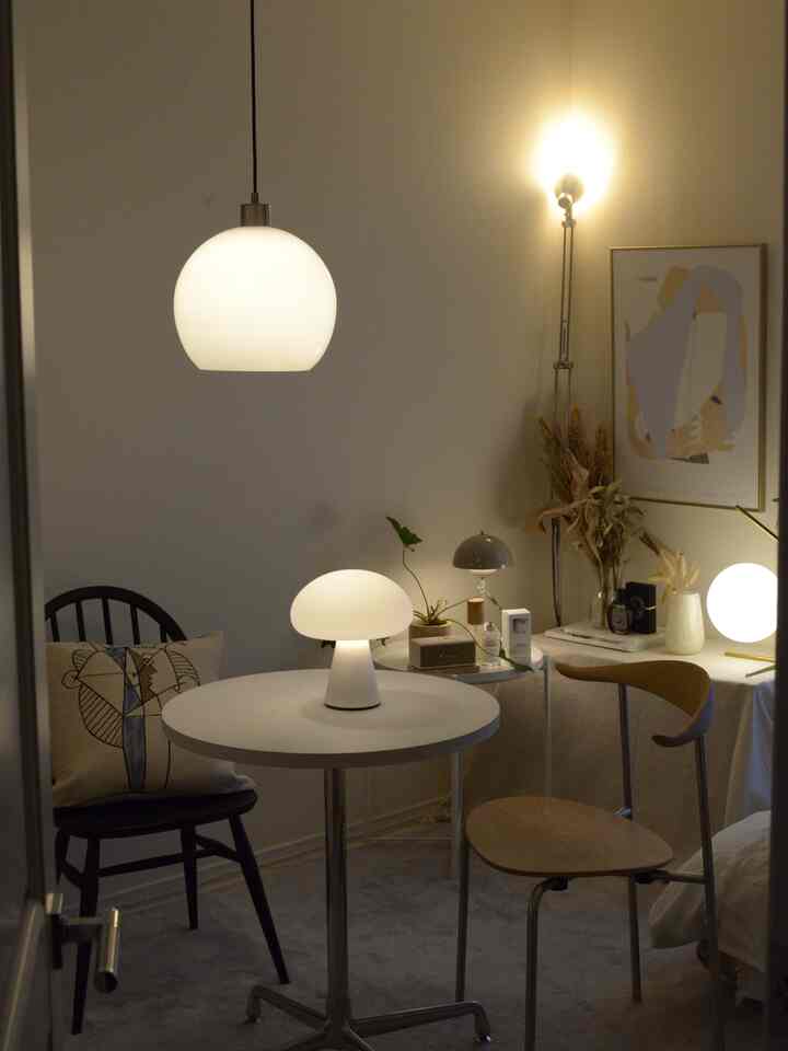 Warm beige compact room featuring simple wooden chairs and round tables with various lamps, creating a cozy atmosphere