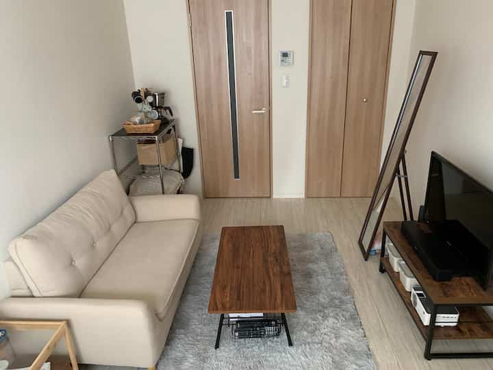 Natural-toned small living room featuring cream sofa, wooden coffee table, and metal rack in a simple setting