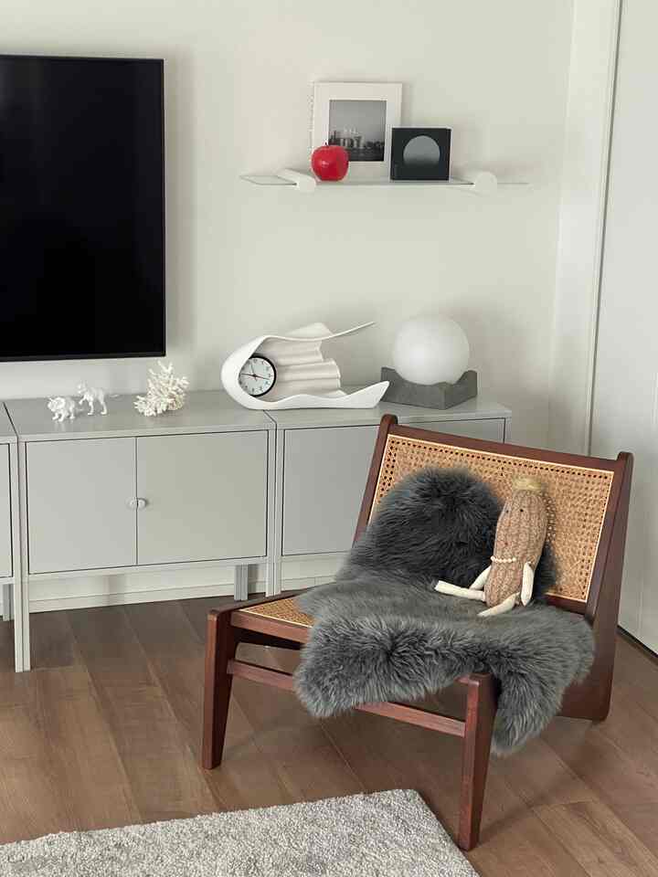 モノトーンのリビング、ジャンヌ・レのチェスカチェアに羊毛ラグとピーナッツのぬいぐるみが置かれた暖かみのあるインテリア