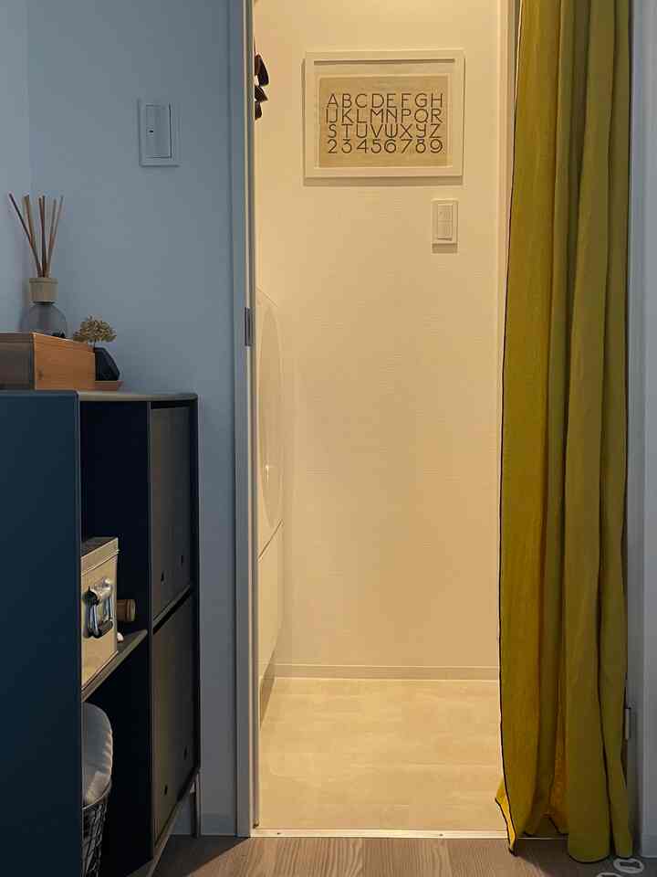 White and natural toned entrance featuring yellow linen curtain and storage shelf, creating warm and practical atmosphere